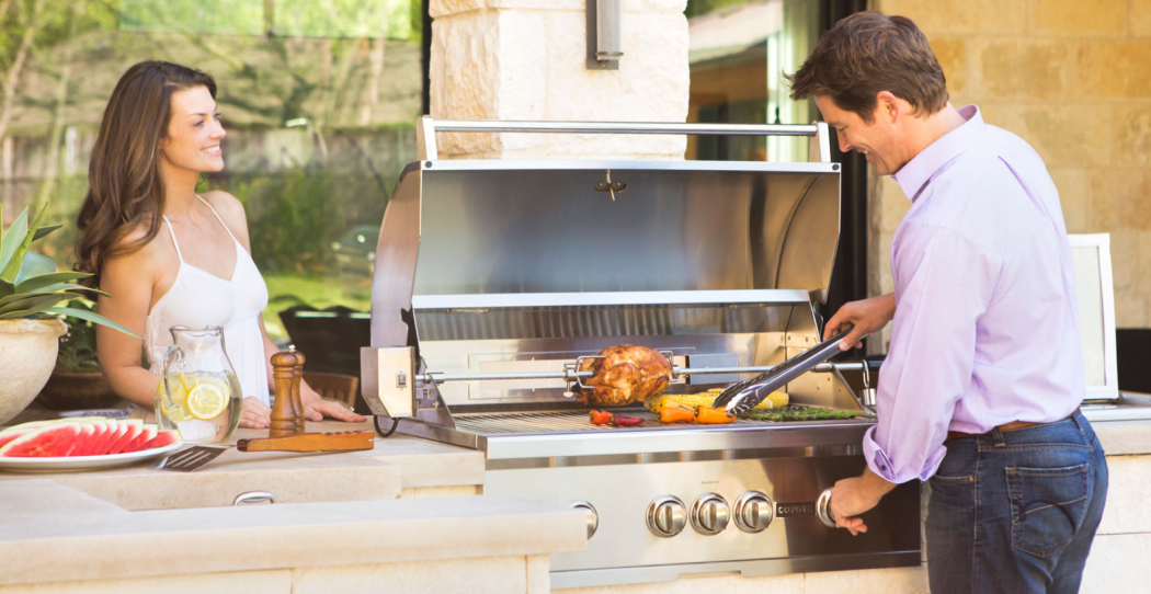 man cooking at a grill with a woman smiling and watching